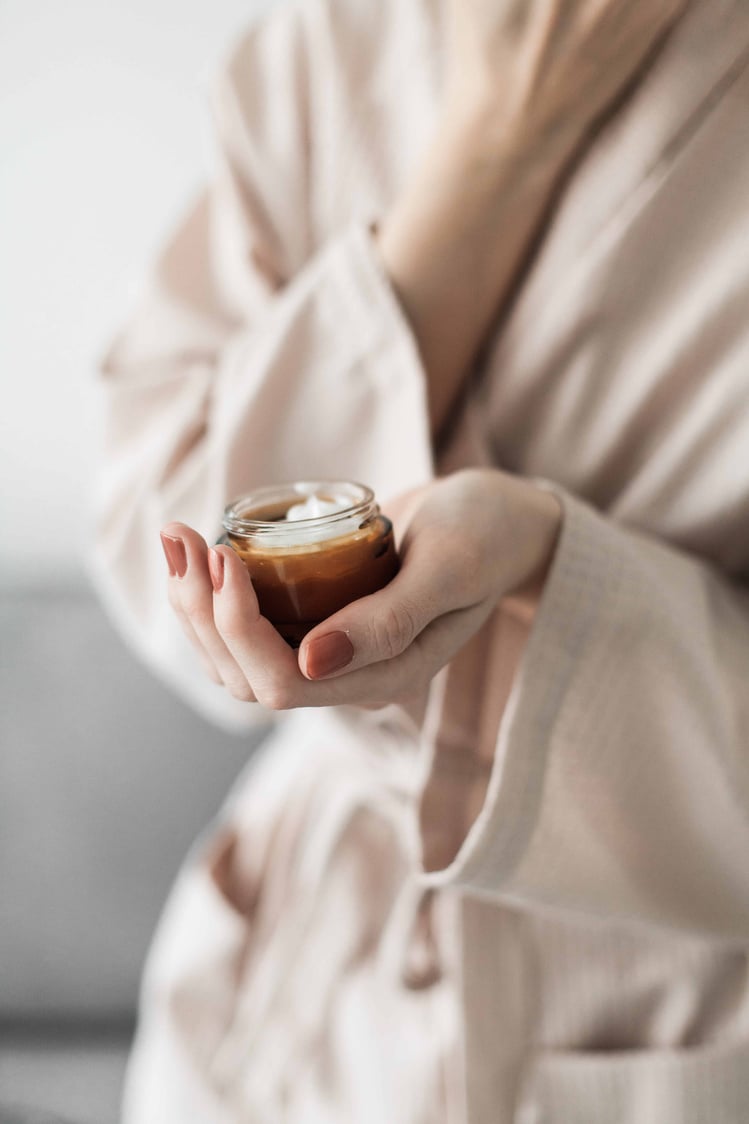 Woman in Bathrobe Holding a Jar of Moisturizer